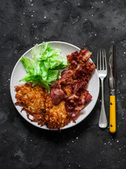 Delicious breakfast, brunch - latkes potatoes, fried bacon and green salad on a dark background, top view