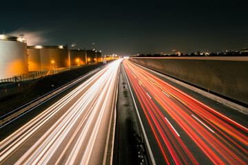 Light trails after long exposure of car traffic on a highway next to industry buildings and a noise barrier at night 