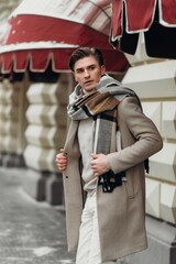  Young man wearing coat walking in the street. Young bearded guy with modern hairstyle in urban background