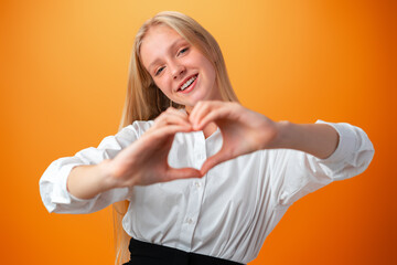 Teen girl showing heart to camera while standing on orange background