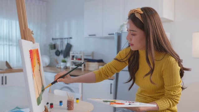 Asian young talented woman artist coloring on painting board in house. 