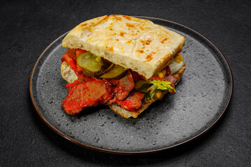 sandwich with smoked meat, pickled cucumbers and herbs. on a plate on a dark background