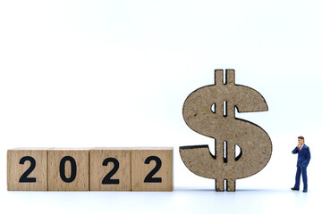 2022 New Year and Business Money Concept. Closeup of businessman miniature figures standing and looking to wood US dollar sign with stack of wooden number block on white background.