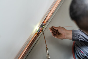 Unknown industrial worker plumber with central heating copper pipes welding using gas torch or...