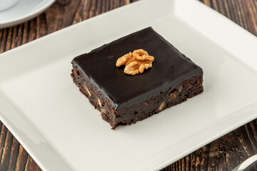 Walnut and dark chocolate brownie on a white porcelain plate on wooden table