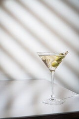 Cocktail vodka martini with green olives on light background with bright beautiful shadows