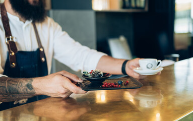 An Anonymous Bartender Putting Cup of Coffee and Dessert on a Golden Bar Counter in a Cafe
