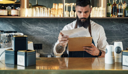 Handsome Barista Doing an Inventory of the Products in a Coffee Shop. 
Serious waiter with a beard...