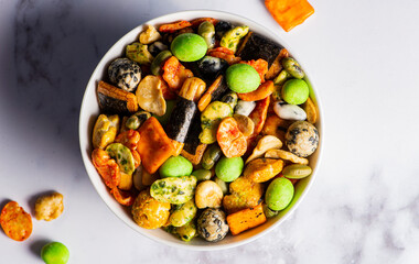 Various Japanese snacks in a wooden bowl close-up. Rice crackers with wasabi and nori, peanuts with sesame seeds, and other snacks. Mix traditional Japanese snack food.