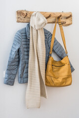 Natural wooden coatrack with jacket, scarf and bag on a white wall. Scandinavian interior style.