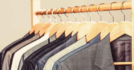 Mens suits in different colors hanging on hanger in a retail clothes store, close-up. Mens shirts,...