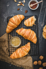 Breakfast scene with croissants, honey, jam and coffee and nuts, black background, top view