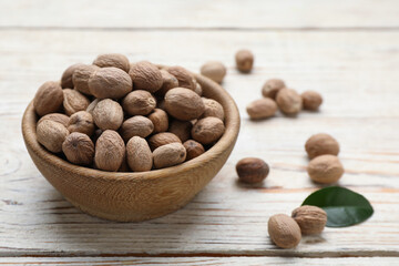 Bowl with nutmeg seeds on white wooden table