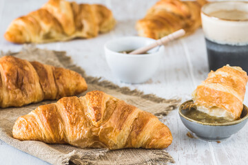 Delicious French croissant on a white wooden table, a cup of coffee and croissants in the background, breakfast scene