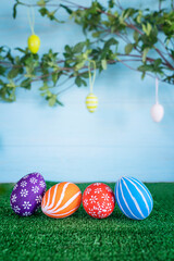 Easter composition with colored Easter eggs at grass against the blue wooden background with branches with green leaves. Easter card