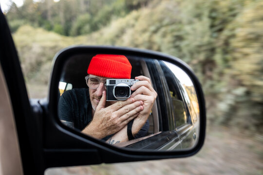 Person taking self portrait in rearview mirror of car while driving