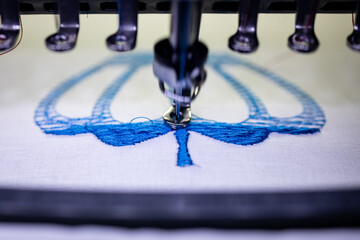 Machine embroidery of a crown on a cotton cloth with blue thread. Blurred photo up close.