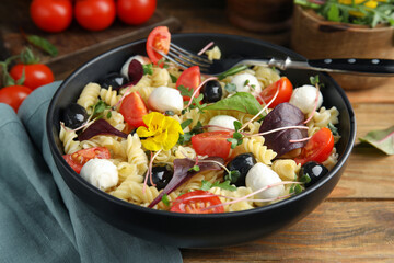 Bowl of delicious pasta with tomatoes, olives and mozzarella on wooden table, closeup