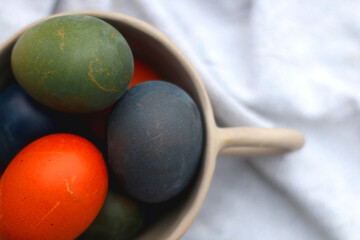Ceramic bowl filled with painted Easter egss in jewel tones. Flat lay.