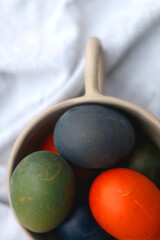 Ceramic bowl filled with painted Easter egss in jewel tones. Flat lay.