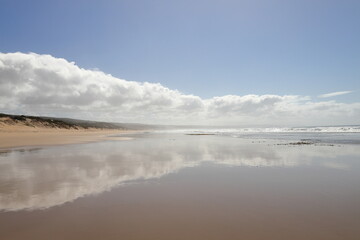 A scenic view on the beach with clouds and reflections.