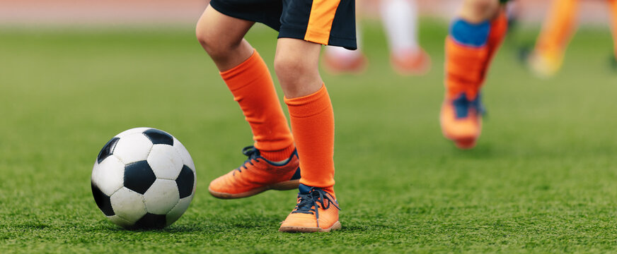 Closeup image of young football player kicking ball. School kids play sports outdoor