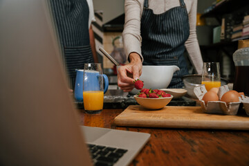 close up of elderly couple baking in kitchen with laptop