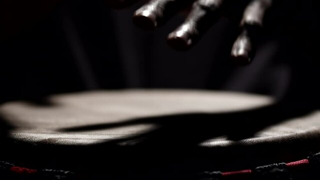 African American man plays an African folk musical instrument, bongo drum, in dark studio filled with smoke, front view, bottom view. Concept of music and performance
