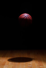 Obraz premium Basketball spot lit suspended in air against a black background above a hardwood maple court floor