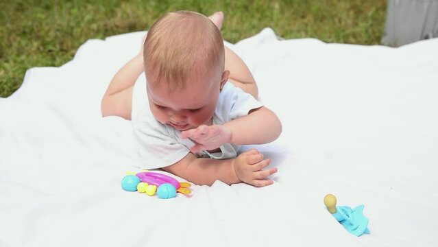 Little newborn girl lying on tummy chewing rattle on blanket, summer day outdoor. Infant having fun outdoors. Infant baby child resting playing learning to crawl. Motherhood teething, babyhood concept
