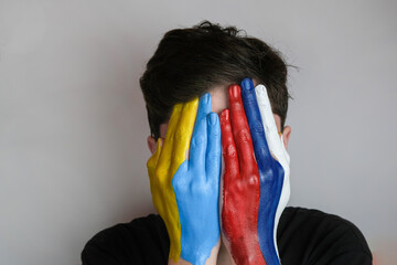 Hand painted in the colors of the flag of Russia and Ukraine. War in Ukraine. Concept of war between Ukraine and Russia. The palms cover the young man's face. 