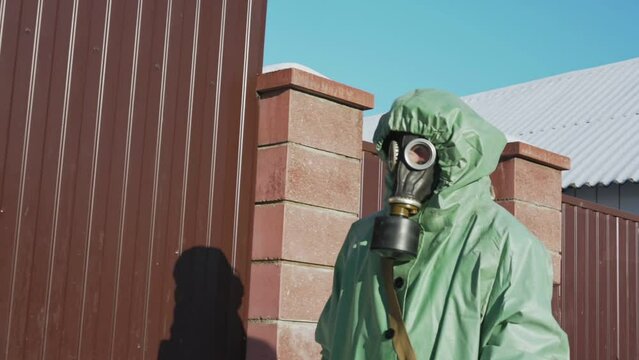 employee of organization for bacteriological and nuclear safety walking near red fence in rural area protecting his body and respiratory organs with protective equipment