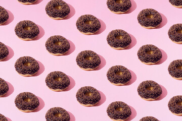 Fototapeta premium Arranged ring donuts whith chocolate glaze and small brown crumbs on a pink pastel background. Minimal concept and design. Pattern.
