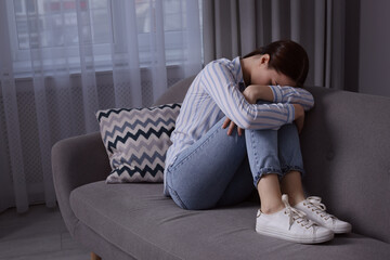 Unhappy young woman on sofa at home, space for text. Loneliness concept