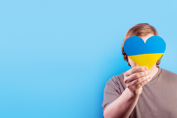 a young Ukrainian guy holds in his hand a heart of a yellow-blue flag isolated on blue background. The concept of participation of the Ukrainian people in the war with Russia. Not war concept