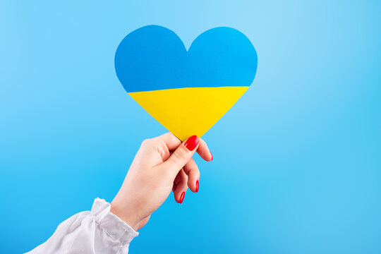 The hand of a young Ukrainian girl holds a heart of a yellow-blue flag on isolated blue background. The concept of participation of the Ukrainian people in the war with Russia. Not war concept