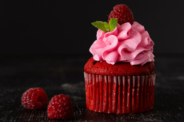 Cupcake red velvet with pink chees cream and raspberries and mint on imitation concrete. Dessert preparation. Copy space. On black background. Delicious delicacy. Muffin with cream. low key. Close up