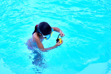 6-8 year old girl with diving goggles and an adventure camera plays in a pool.