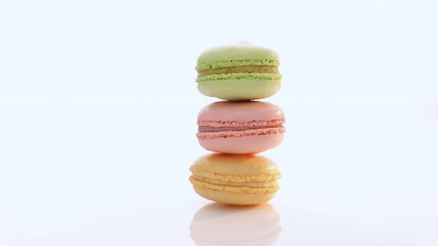 Vertical stack of three macarons against a bright white background. Sweet colorful macarons isolated on white background. Tasty colourful macaroons. High quality video 4k uhd.