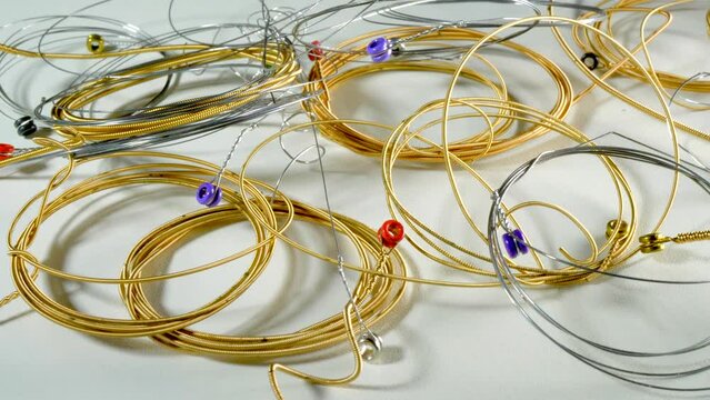 Closeup circular dolly shot of used steel guitar strings &ndash; plain and brass wound &ndash; in a coiled pile, to be discarded or used as spares. 