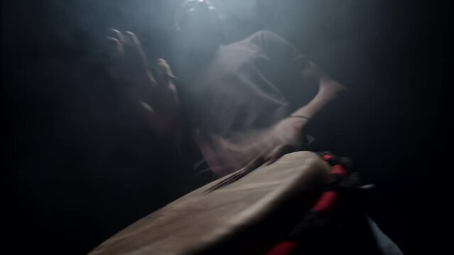 African American man plays an African folk musical instrument, bongo drum, in dark studio filled with smoke, front view, bottom view. Concept of music and performance