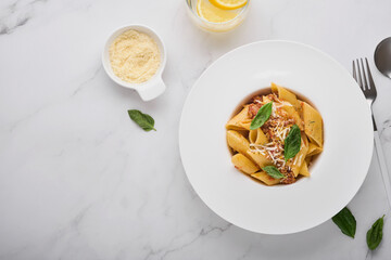 Bolognese Penne Pasta. Tasty appetizing classic italian penne pasta with parmesan cheese, basil and Bolognese sauce in white plate on plate on stone table. Traditional dish of Italian cuisine Top view