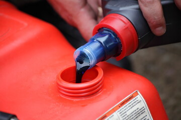 Naklejka premium Pouring 2 Т oil into gasoline. Preparation of a fuel mixture for a two stroke outboard motor.