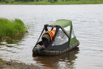 Obraz premium A fisherman climbs into an inflatable boat with a bow awning on the water. Fishing in rainy weather.