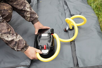 A man hands pumps up an inflatable boat with electric air pump before trip - obrazy, fototapety, plakaty