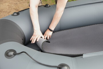 White male hands lay a protective carpet in an new inflatable boat with a soft bottom.