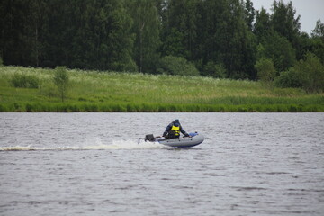 Fototapeta na wymiar Small inflatable boat floating on European river on green forest on far shore background at summer day. Active outdoor recreation on the water.