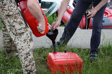 Men pour gasoline from a red plastic fuel tank on inflatable motorboat background. Refueling for trip on a motor boat.