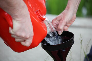 A man hands pours gasoline from a plastic gas tank through a funnel. Danger of ignition of fuel...