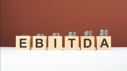 EBITDA text on wooden blocks with coins on brown background